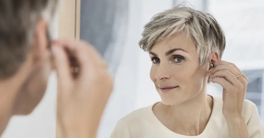 Une audioprothésiste ajuste un appareil auditif discret sur l’oreille d’une patiente
